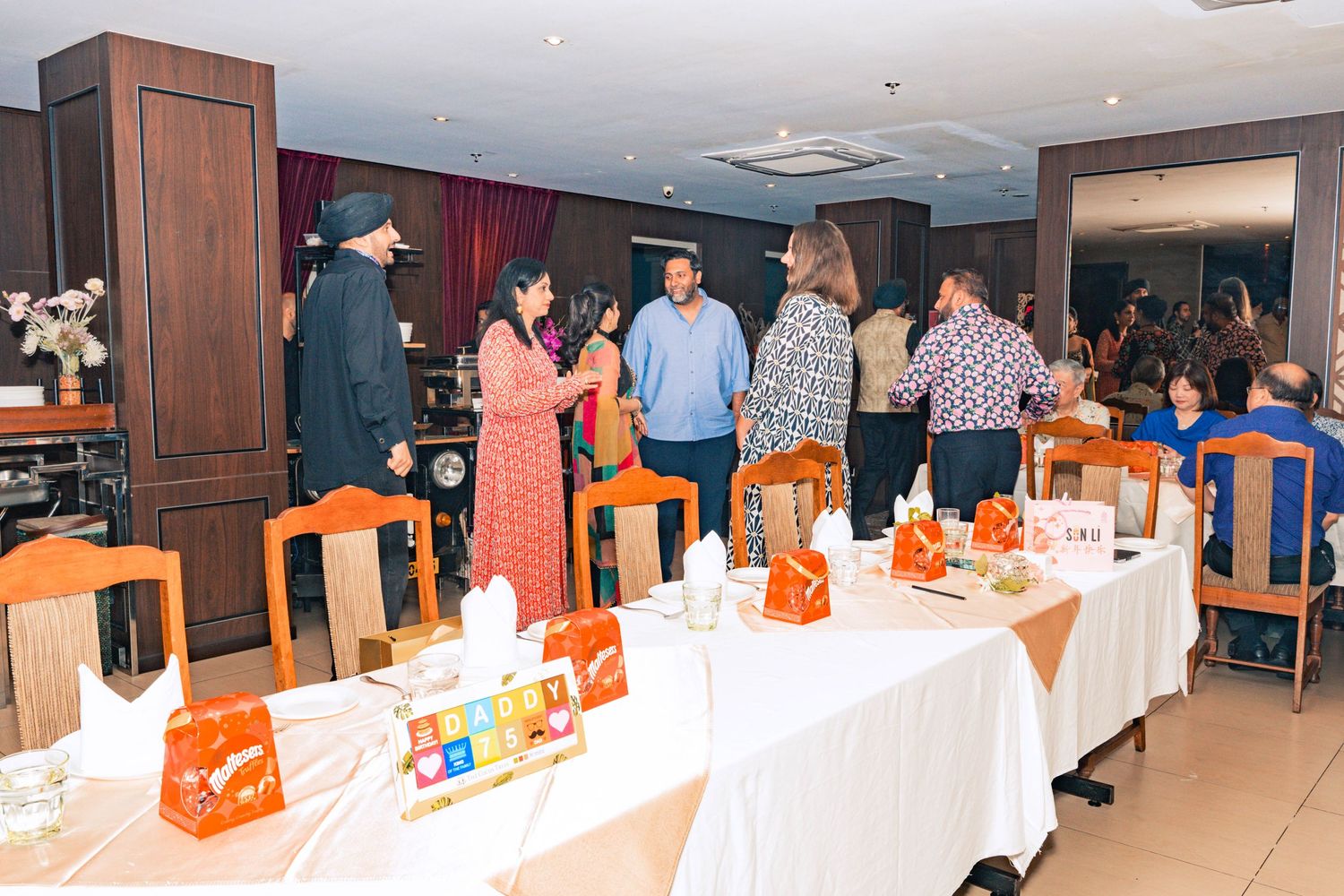 Dining room setup with orange chairs and white tablecloths decorated with gift bags.