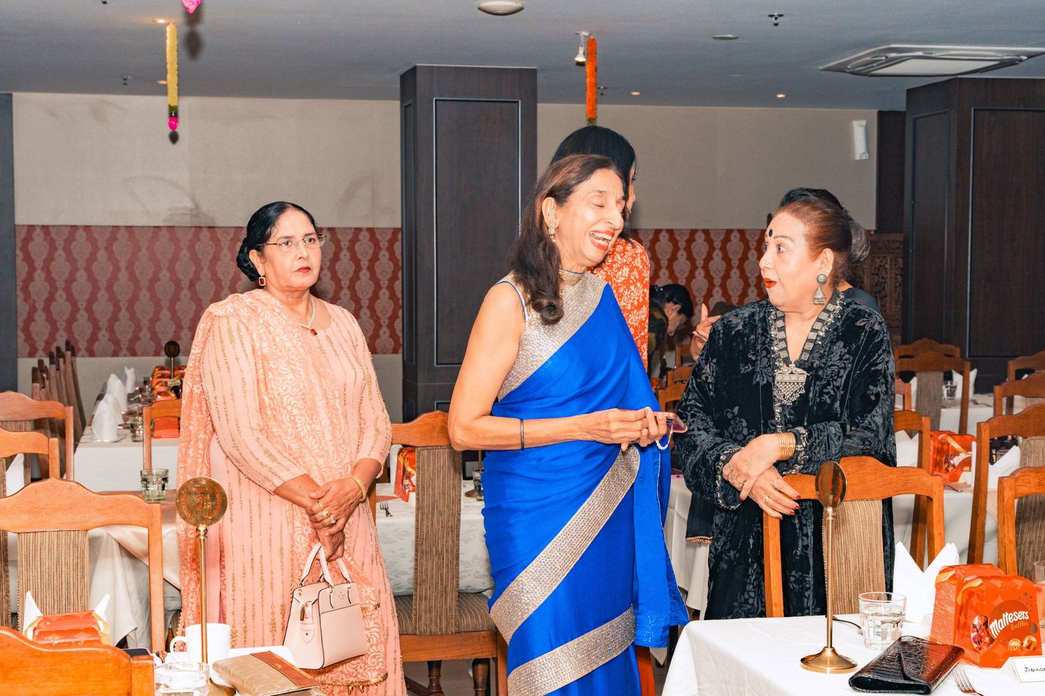 Three people chatting in traditional Indian attire at an indoor event.