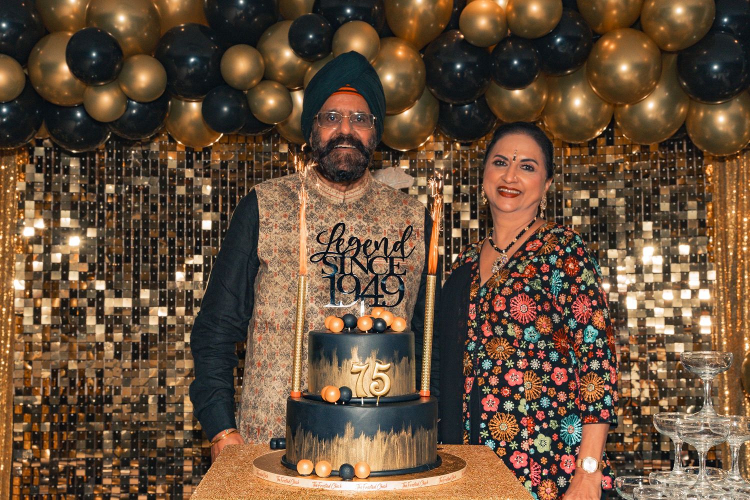 Celebration with black and gold balloon arch decorations and an elegant tiered cake on display.