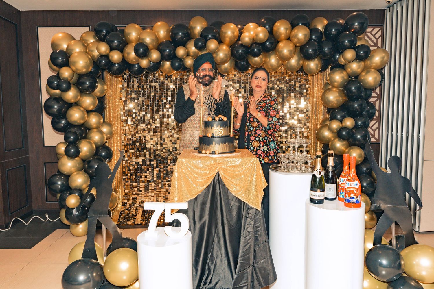 Party setup with black and gold balloon garland and decorative displays on pedestals.