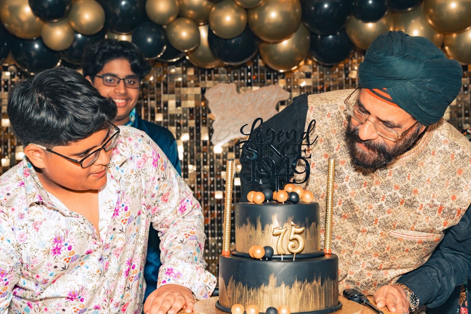 Celebratory gathering around a dark-colored tiered cake with gold accents.