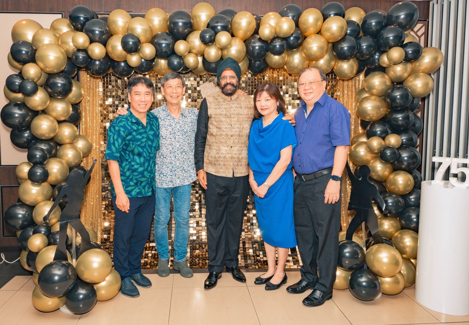 Group photo against a backdrop of black and gold balloon garland at formal event.