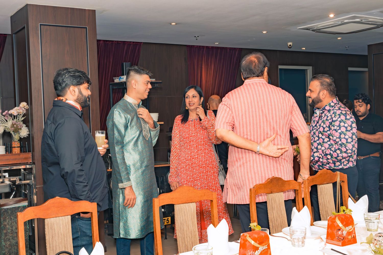 A group chatting and socializing at a dining event with orange chairs and table settings.
