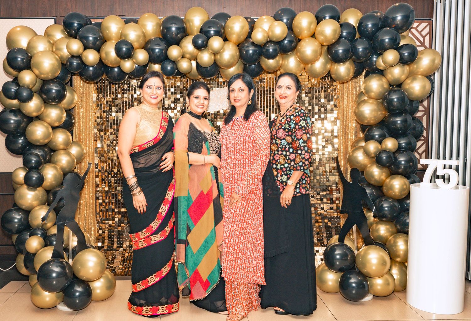 Elegant party setup with black and gold balloon arch decorations against a patterned backdrop.