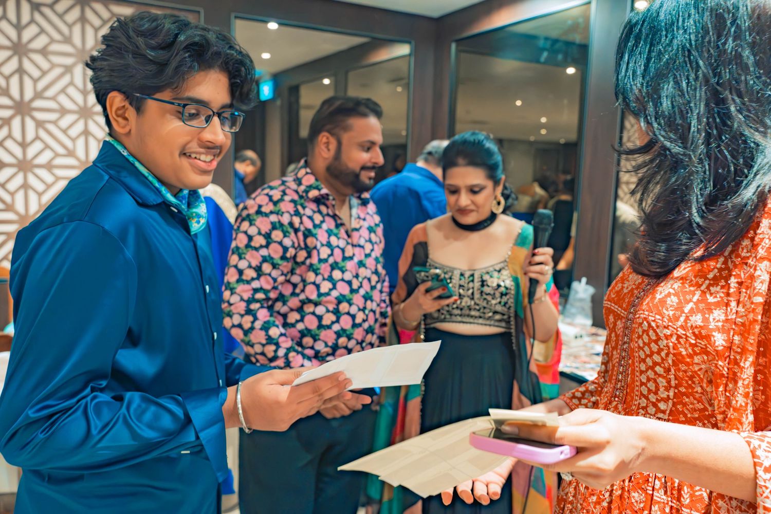 People in traditional Indian attire exchange papers at an indoor gathering event.