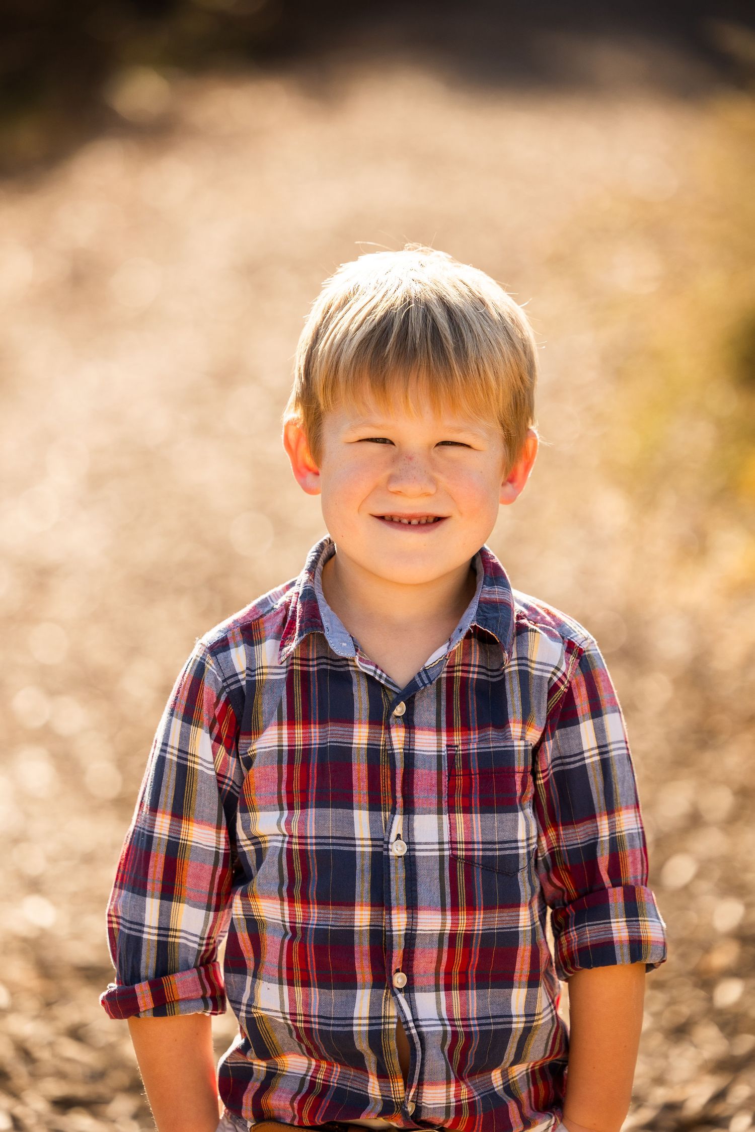 Young child in plaid shirt smiling during autumn outdoor portrait session.