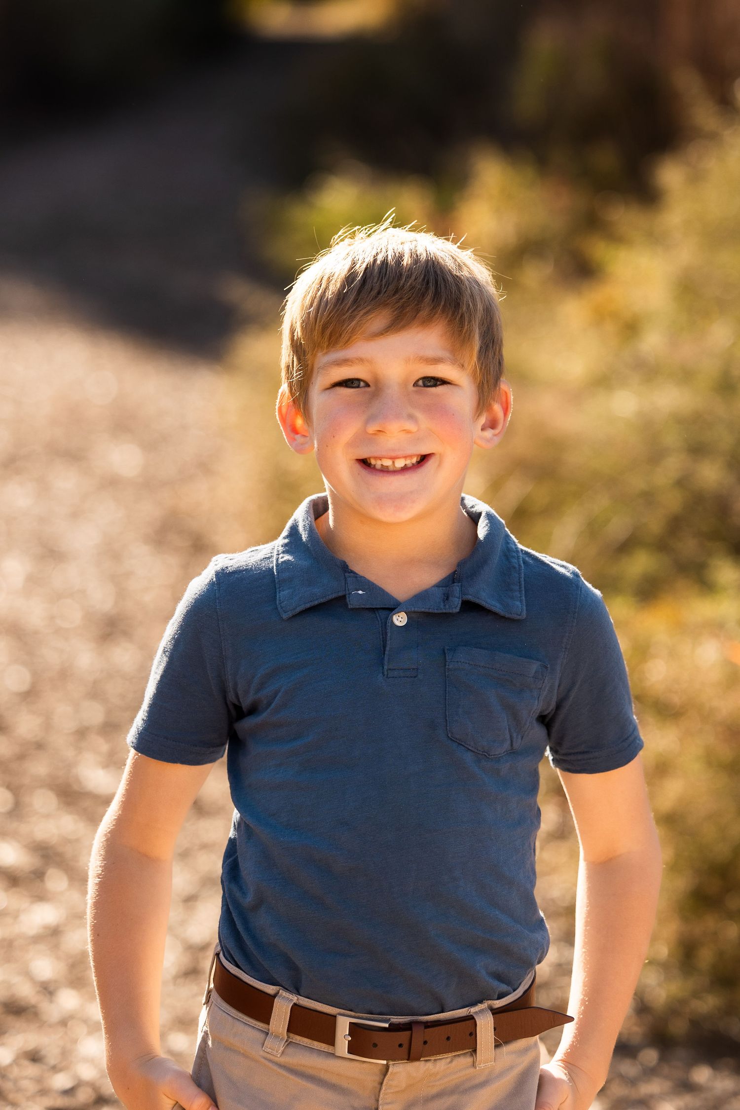 Child in blue polo shirt smiling during sunny outdoor photoshoot.