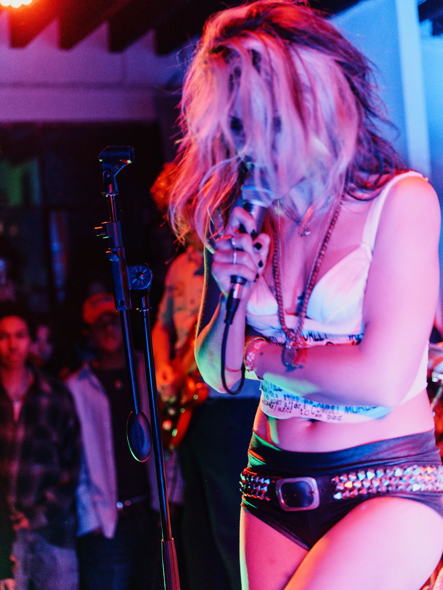 Live music performance with dramatic lighting showing performer on stage with microphone in concert setting.