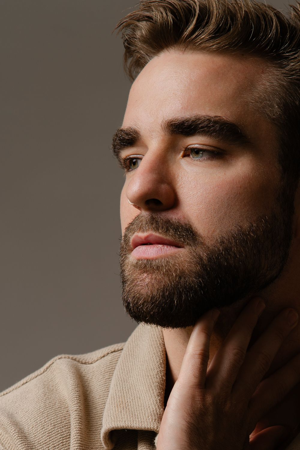 Close-up studio portrait of a stylish man in beige sweater with well-groomed beard against neutral background.
