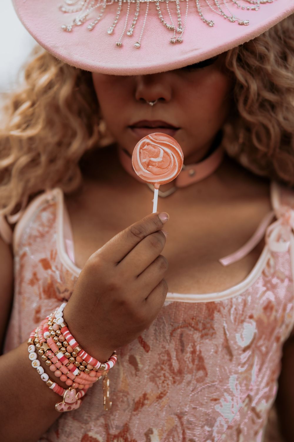 A person in pink lace holds a heart-shaped lollipop while wearing colorful beaded bracelets.