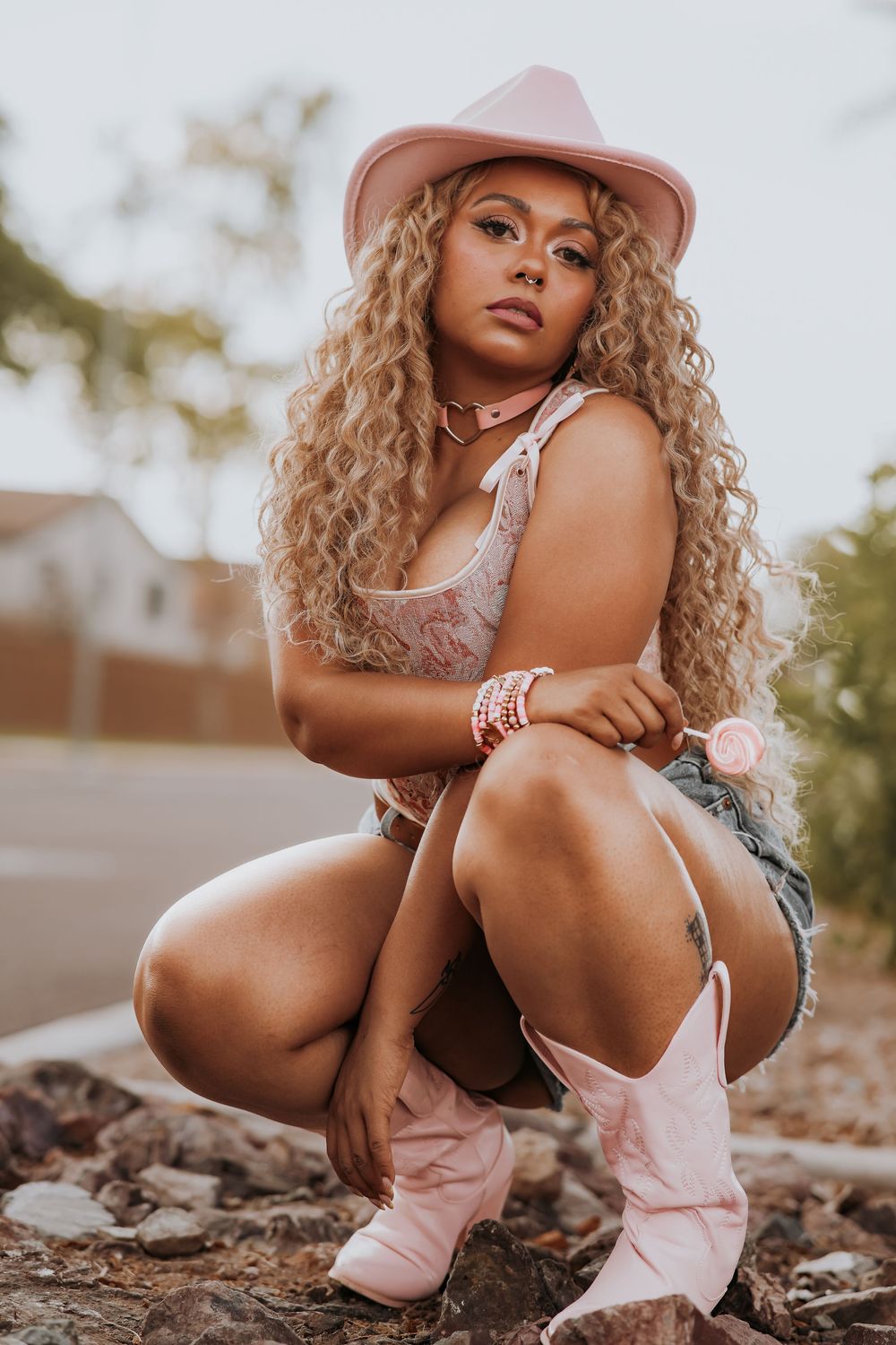 Stylish western-inspired portrait featuring pink cowboy boots, denim shorts, and a matching pink hat in warm sunset lighting.