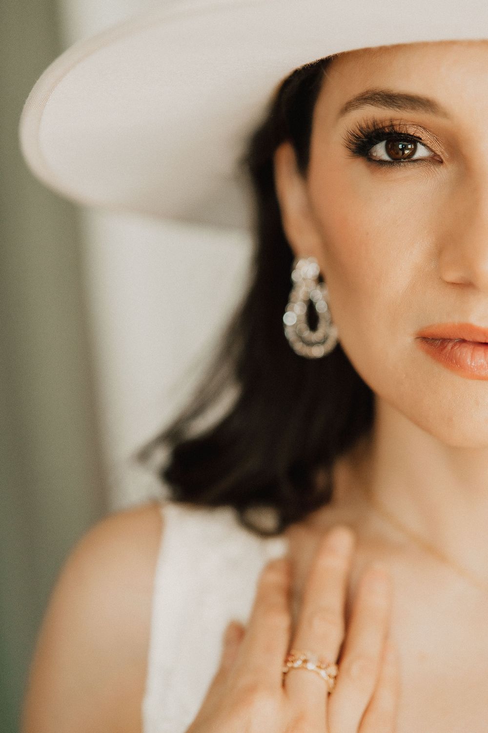 Close-up beauty portrait showing a sparkly diamond earring, coral lipstick, and natural makeup in warm lighting.