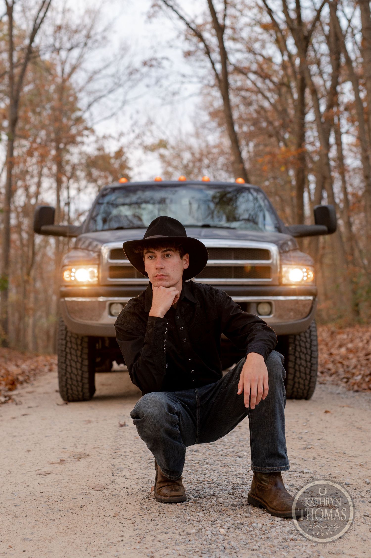 A Dodge Ram truck with headlights on and someone in western attire crouching in front.