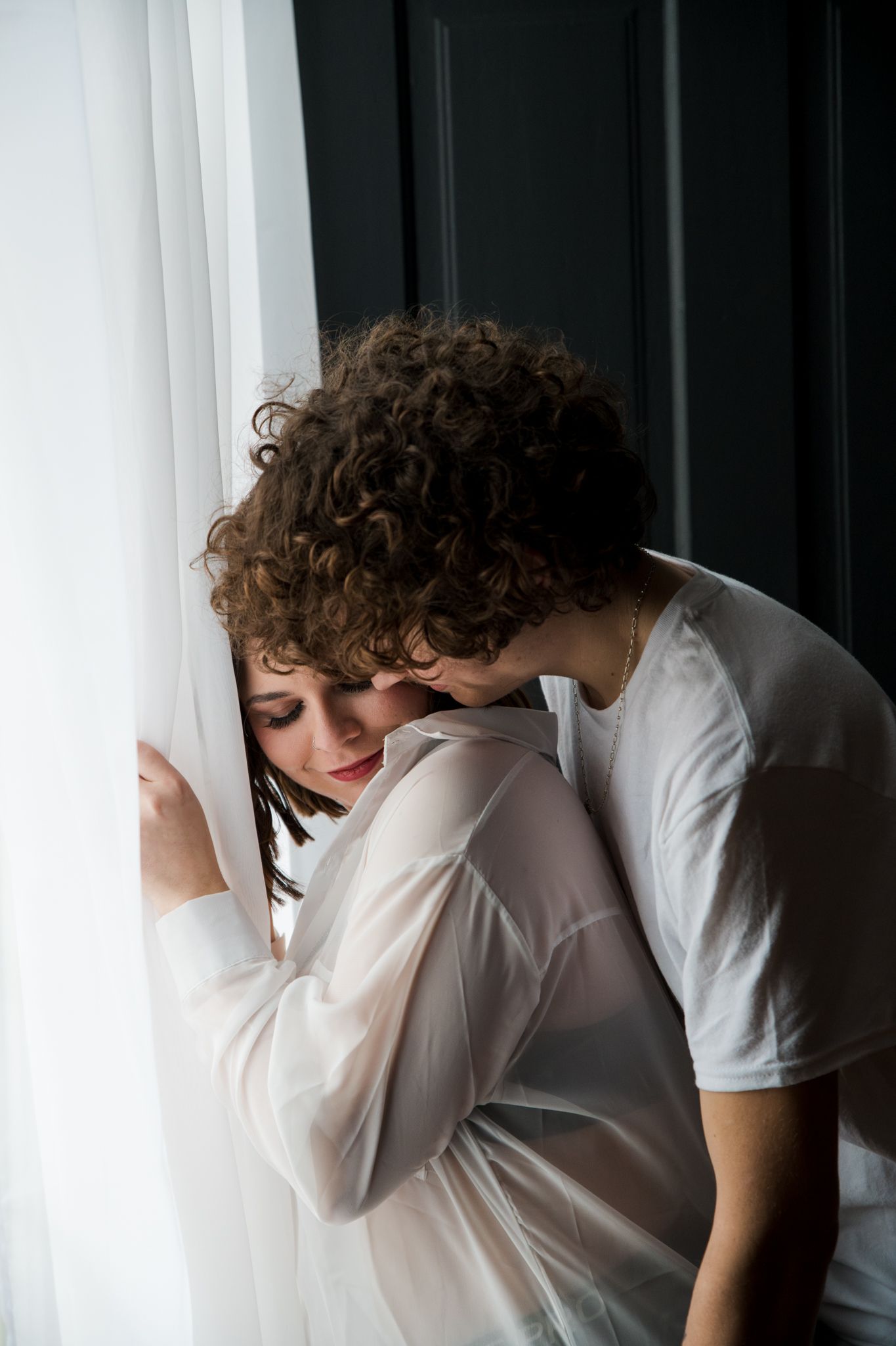 Artistic portrait by window with soft natural lighting and sheer fabrics.