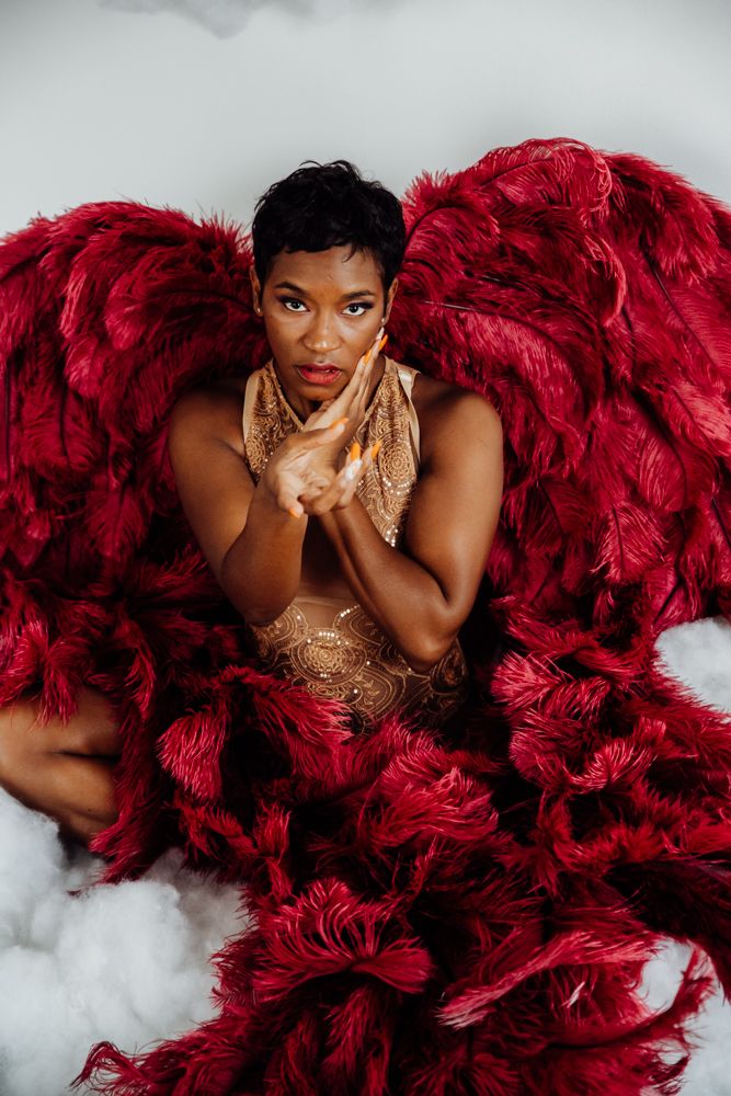 Glamorous fashion photo with luxurious red feathers and a gold sequined dress against a light gray background.