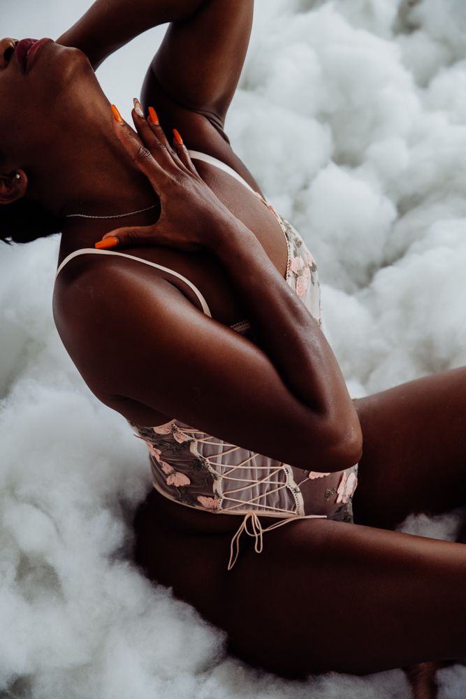 Artistic portrait of person in lace corset posing against cloudy white background with dramatic lighting and shadows.