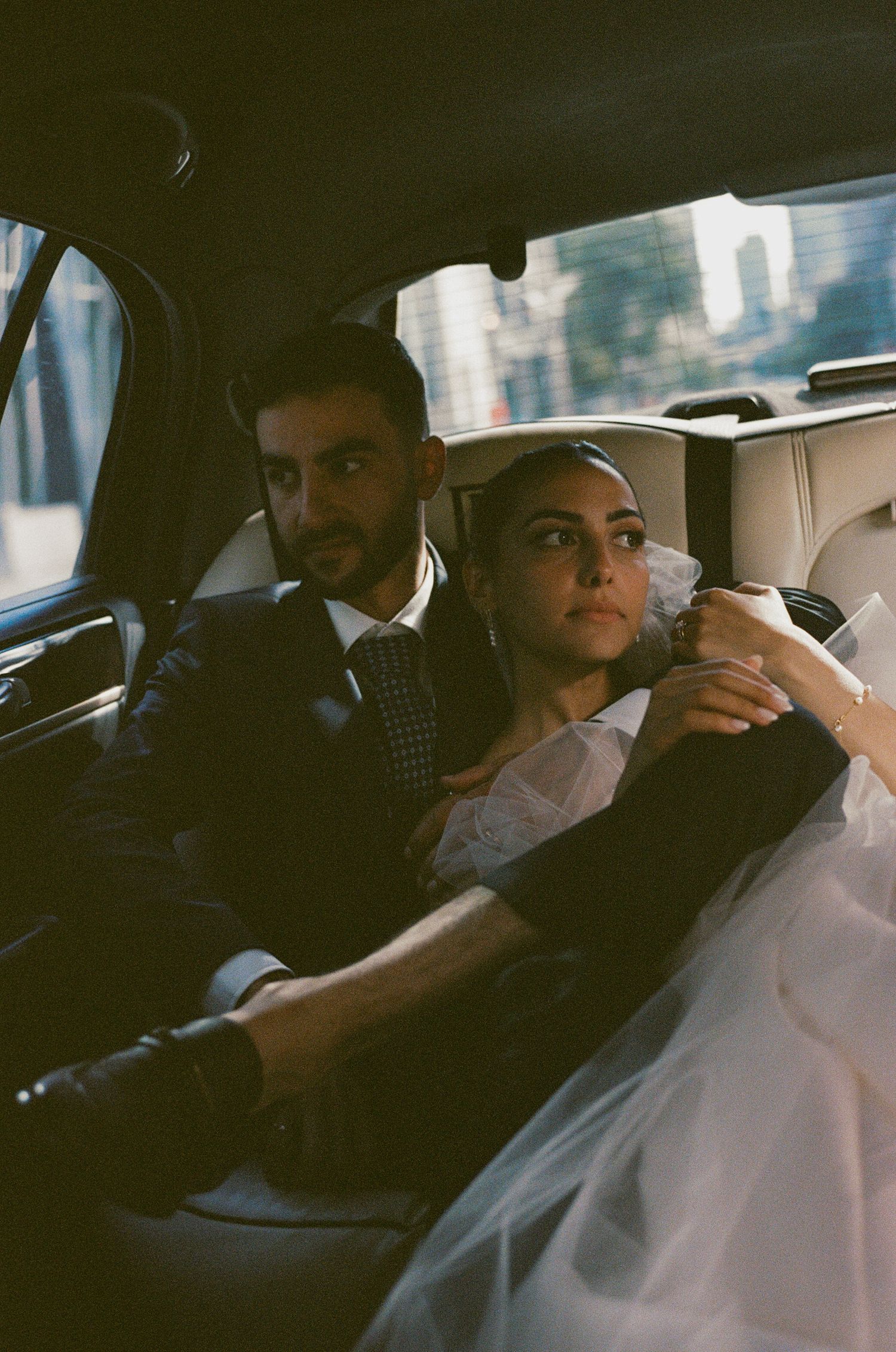 Candid photo of newlyweds sitting together in back seat of car after wedding ceremony.