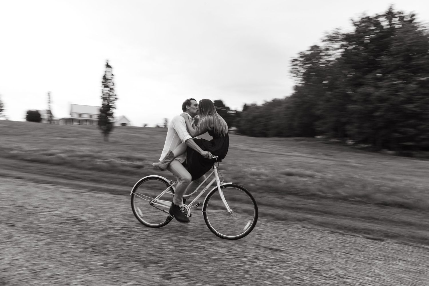Playful couple riding together on bicycle in black and white motion shot.