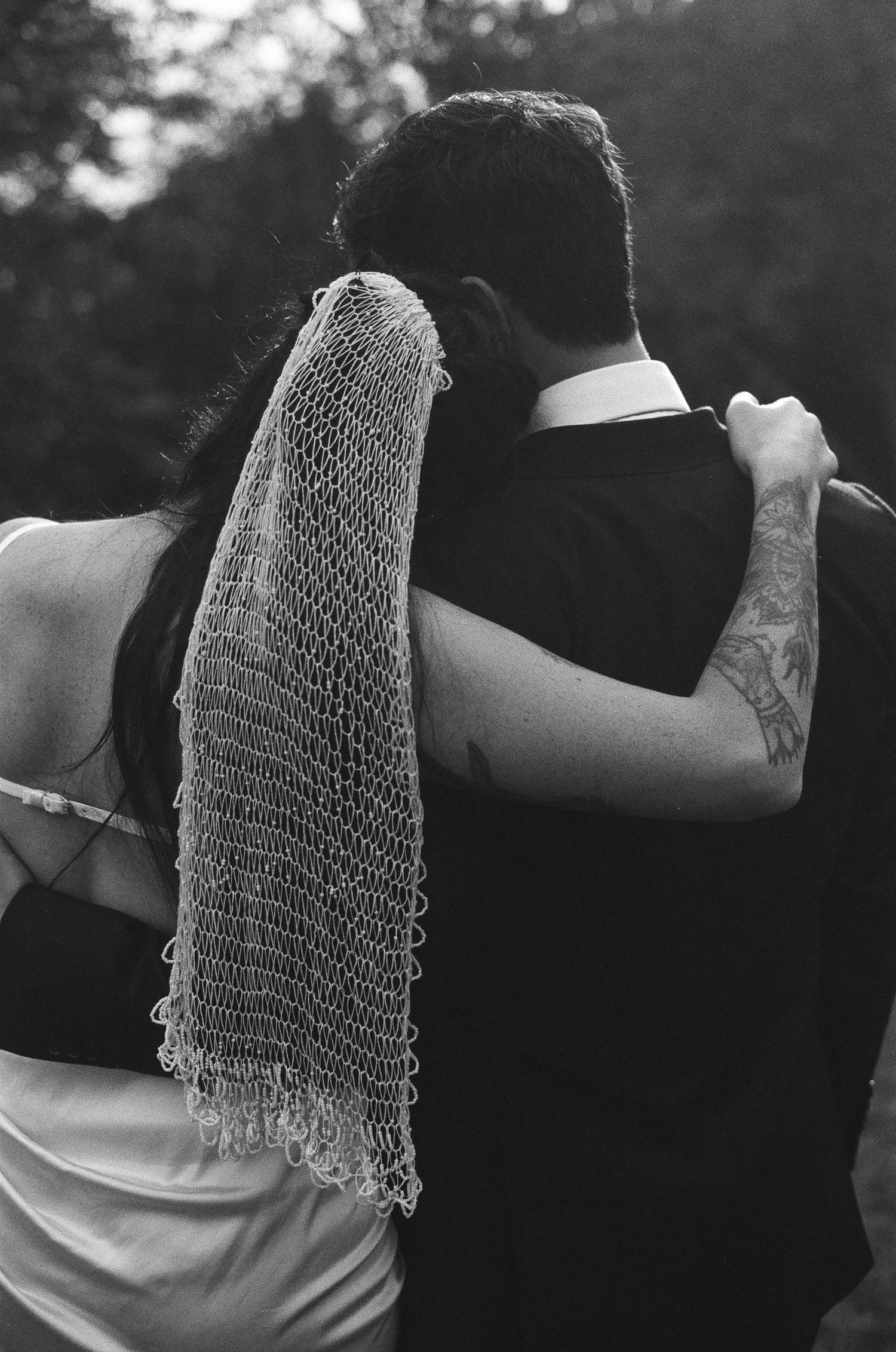 A black and white photo of a couple dancing together, with a delicate lace veil draping over their embrace.