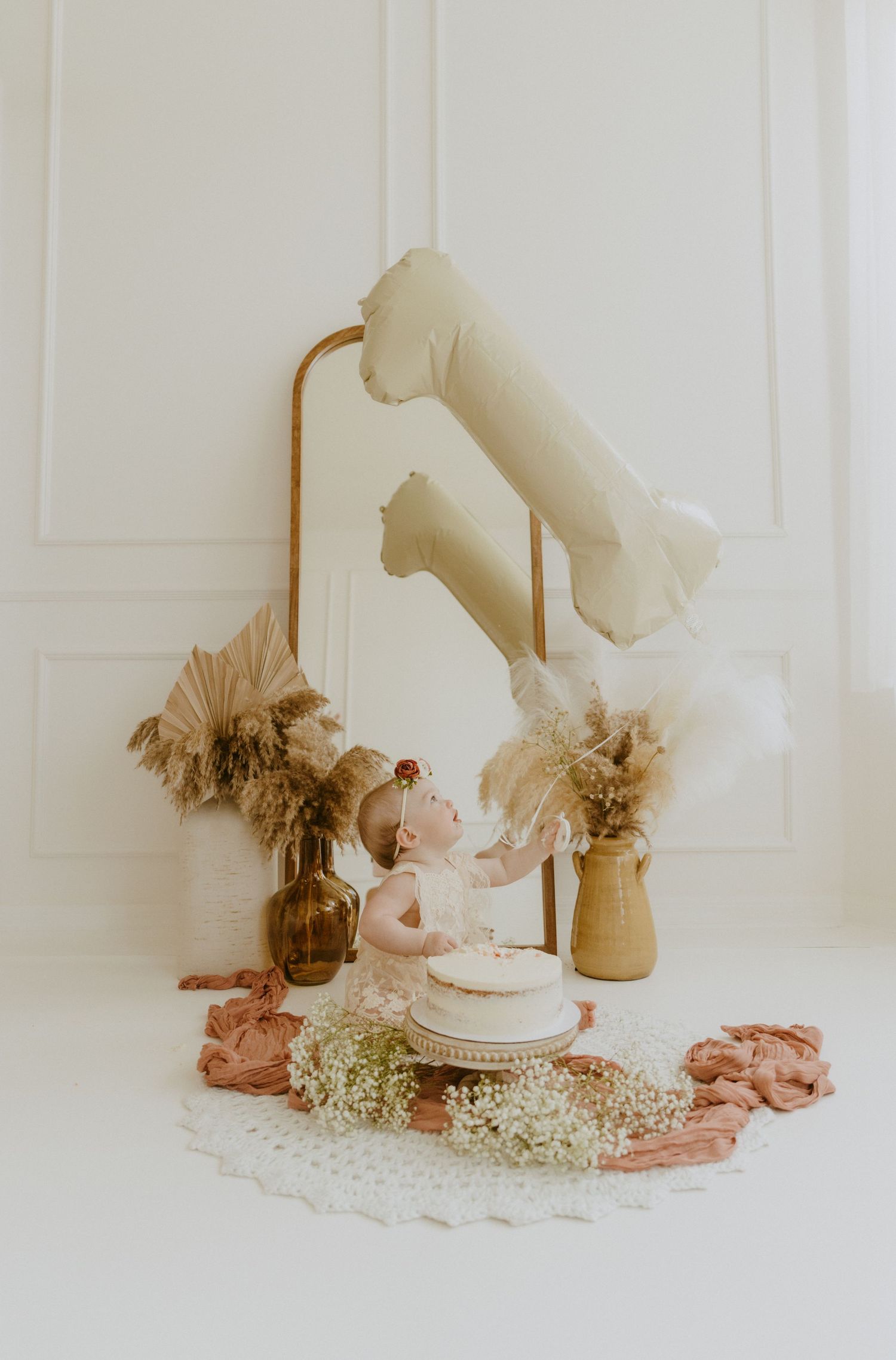 Vintage-inspired baby cake smash setup with pampas grass decor and neutral tones against white backdrop.