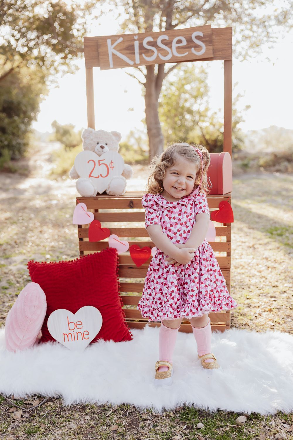 Valentine's themed photo setup with kissing booth sign, teddy bear, and red decorations.