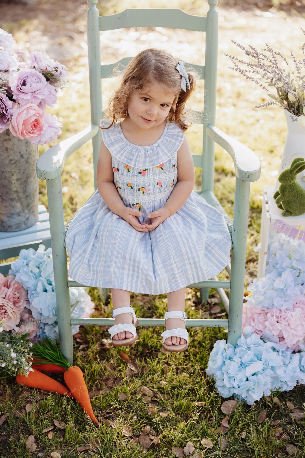 Sweet springtime scene with a light blue dress on a mint green chair surrounded by pink roses and hydrangeas in a garden.