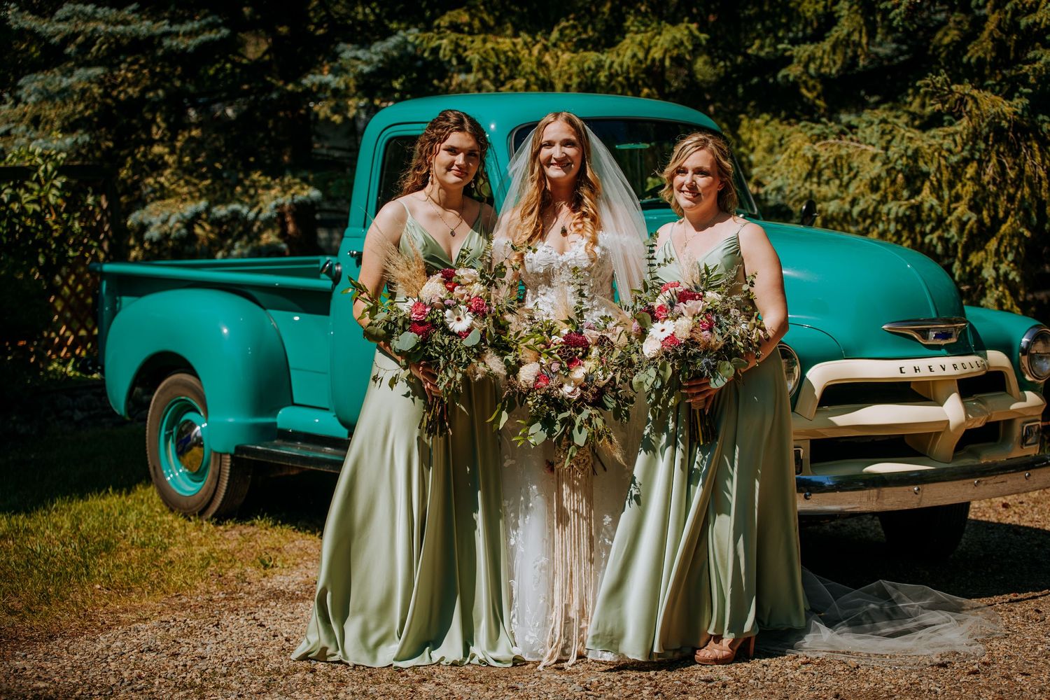 Wedding party poses in front of a vintage turquoise pickup truck holding beautiful floral bouquets.