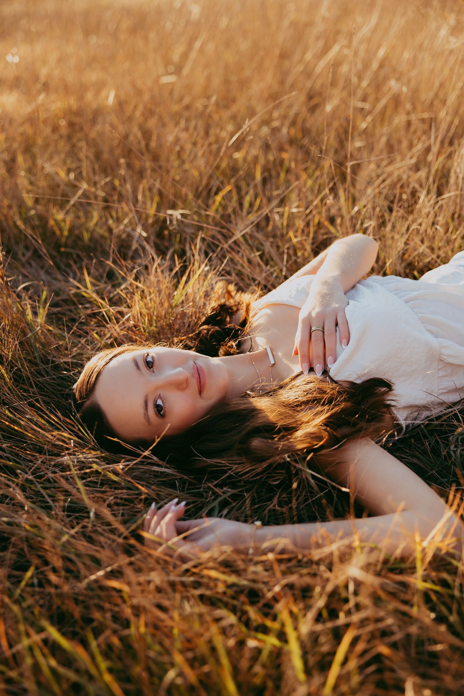 Person lying in golden wheat field at sunset wearing white clothing while bathed in warm sunlight.