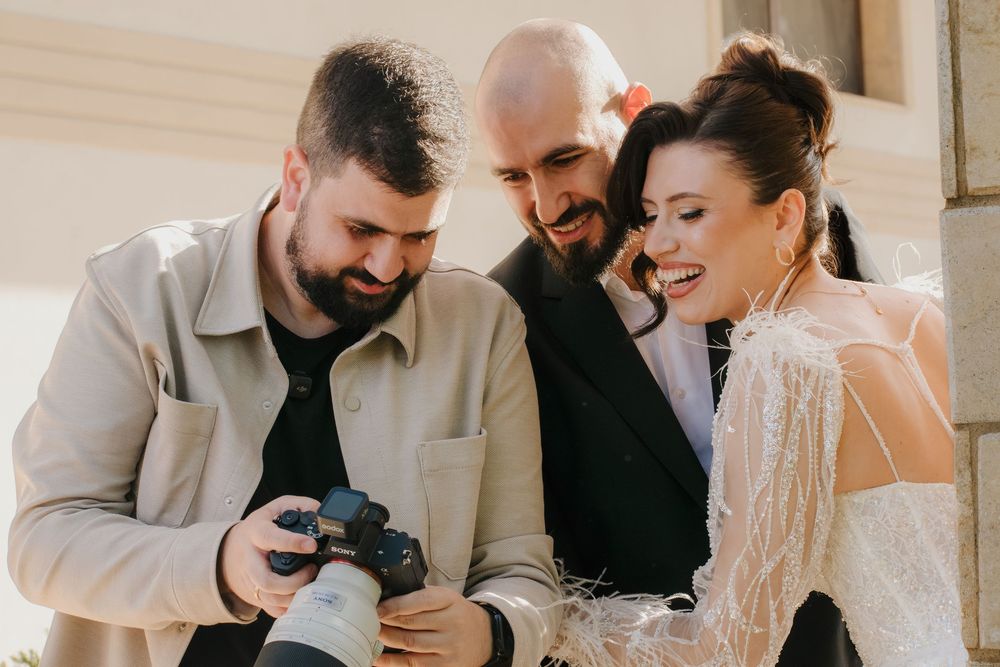 Wedding photographer shows couple images on camera display during outdoor photoshoot on sunny day.