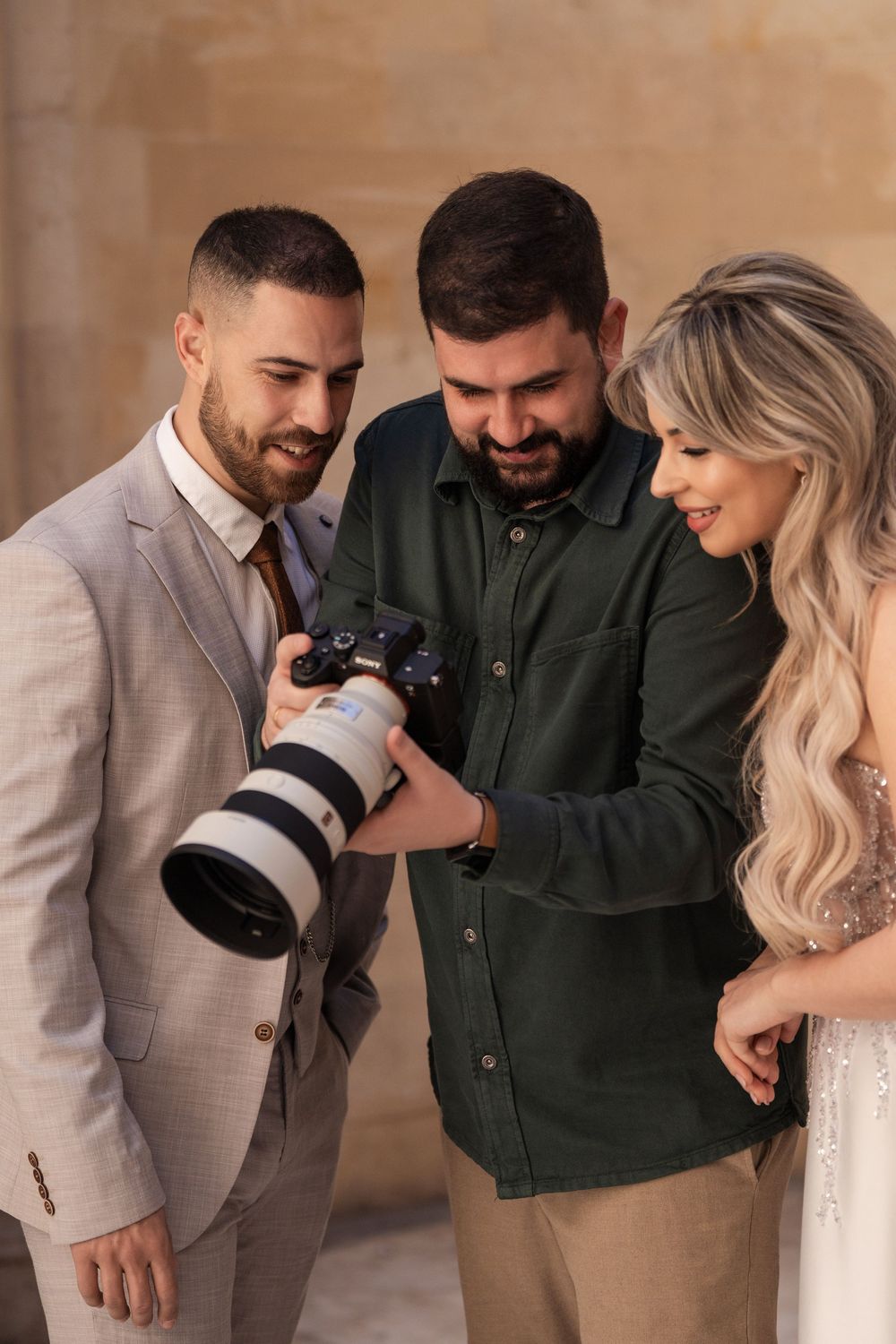 Professional photographer shows wedding photos on camera display to couple in elegant attire.