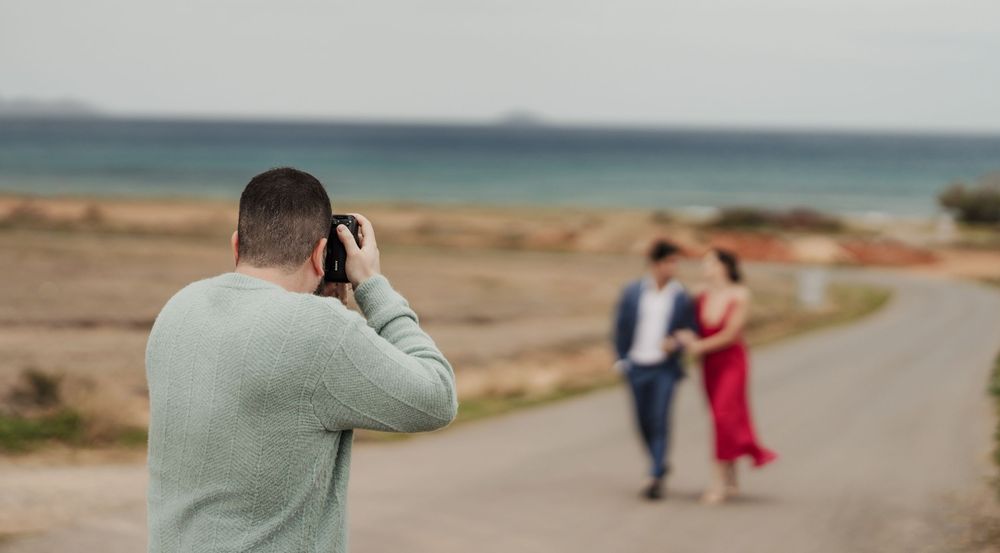 Photographer captures a couple in formal attire walking along a scenic coastal path at sunset.