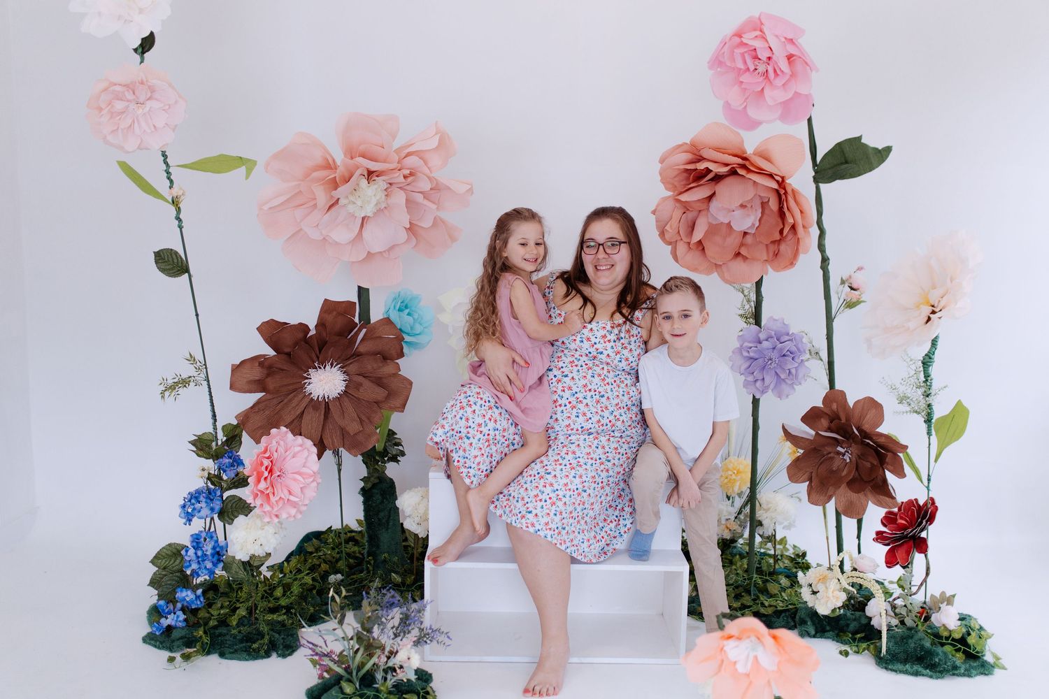 Thalie photography Mother sitting with two young children in front of colorful oversized paper flower backdrop in studio.