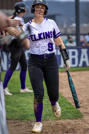 Softball player in Elkins, Arkansas uniform celebrates with teammates in the dugout.