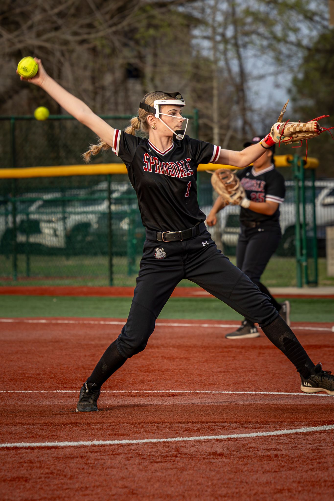 Softball pitcher from Springdale Bulldogs performs a windmill pitch on a dirt field.