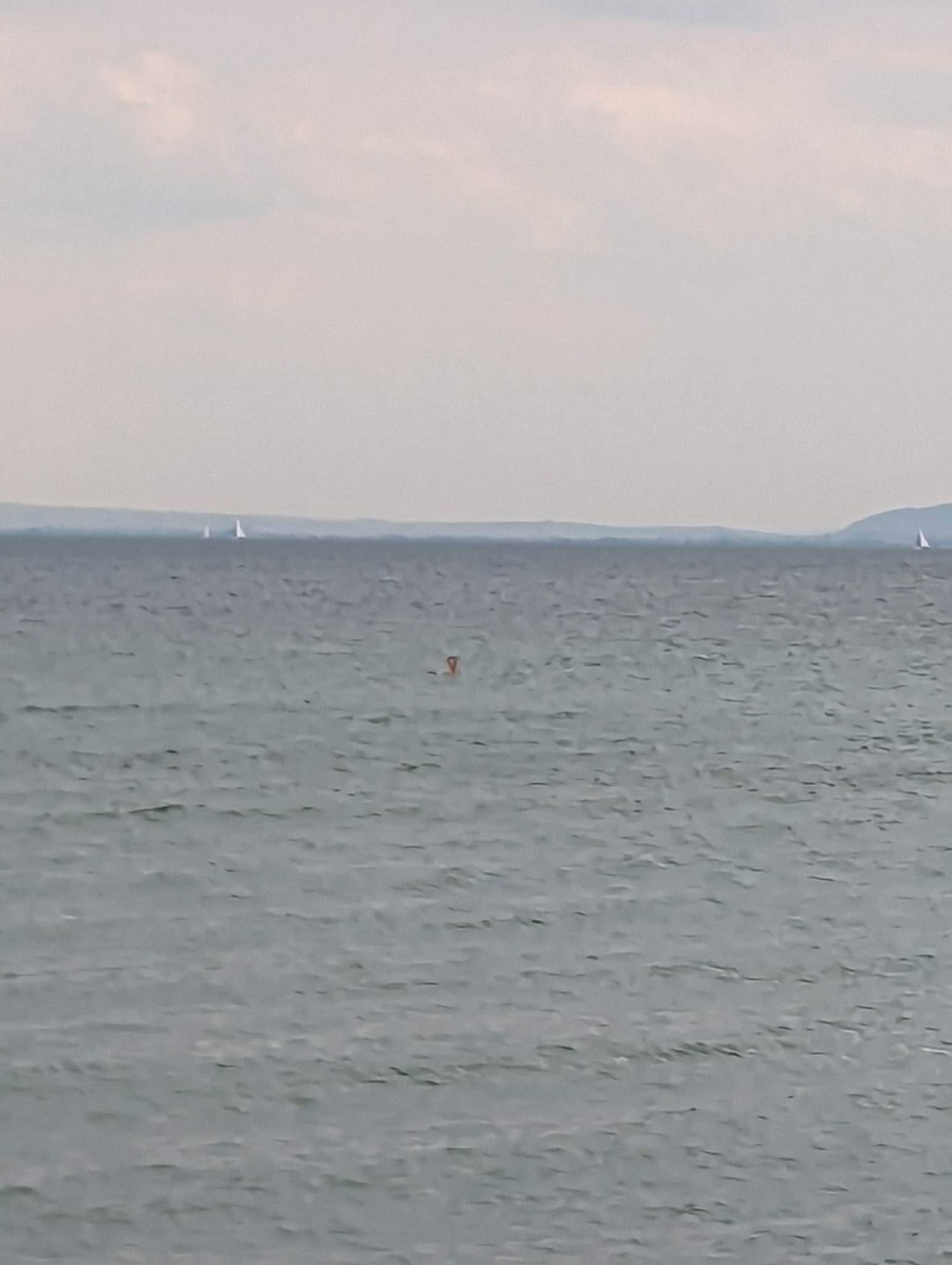 Distant sailboats dot the horizon on a gray, overcast day at sea with choppy waters.