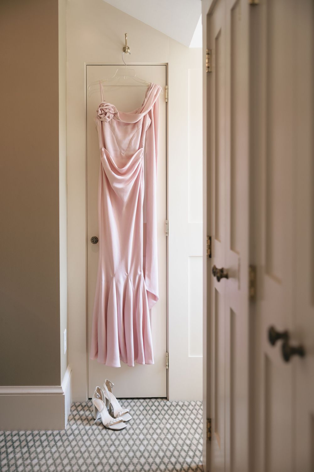 A pink silk slip dress hangs on a white door in a minimalist interior setting.