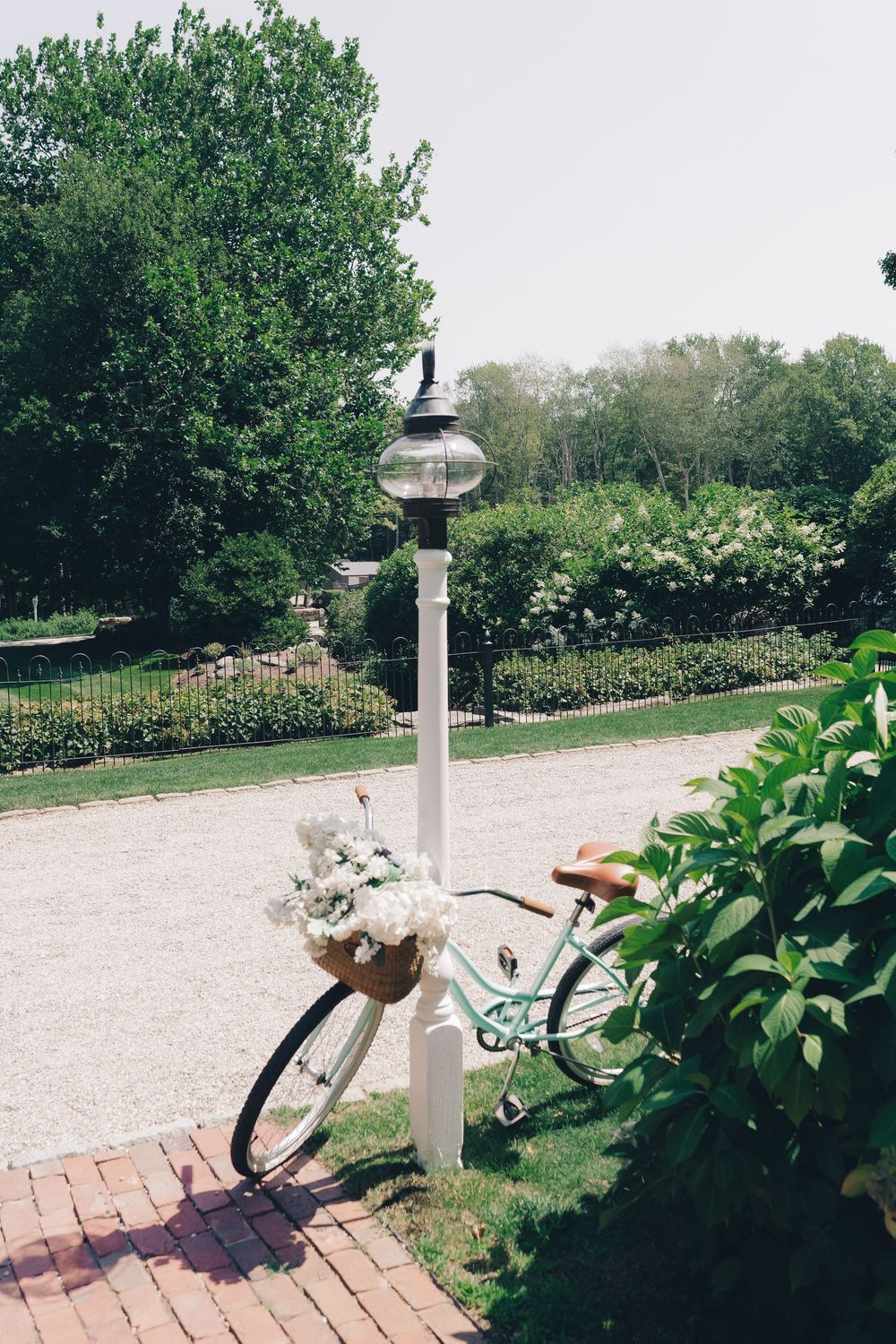 Vintage bicycle leans against a white post on a brick path in a garden setting.