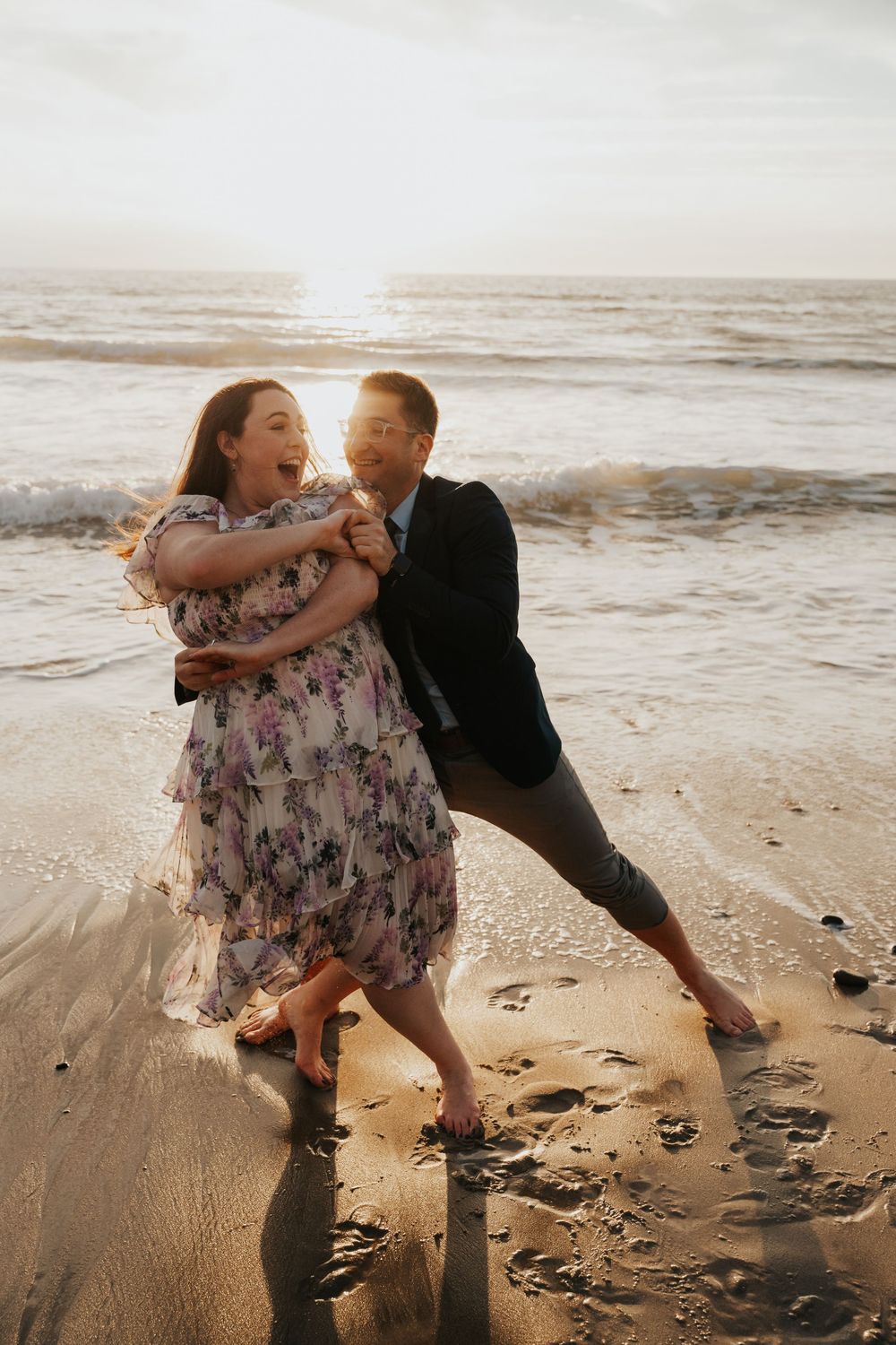 A couple shares a playful and romantic moment together on a sandy beach at sunset.