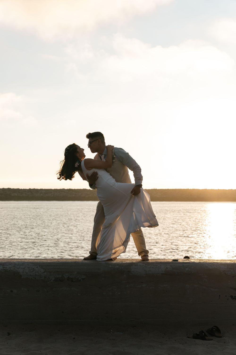 Silhouetted couple sitting together on beach at sunset sharing intimate moment by water's edge.