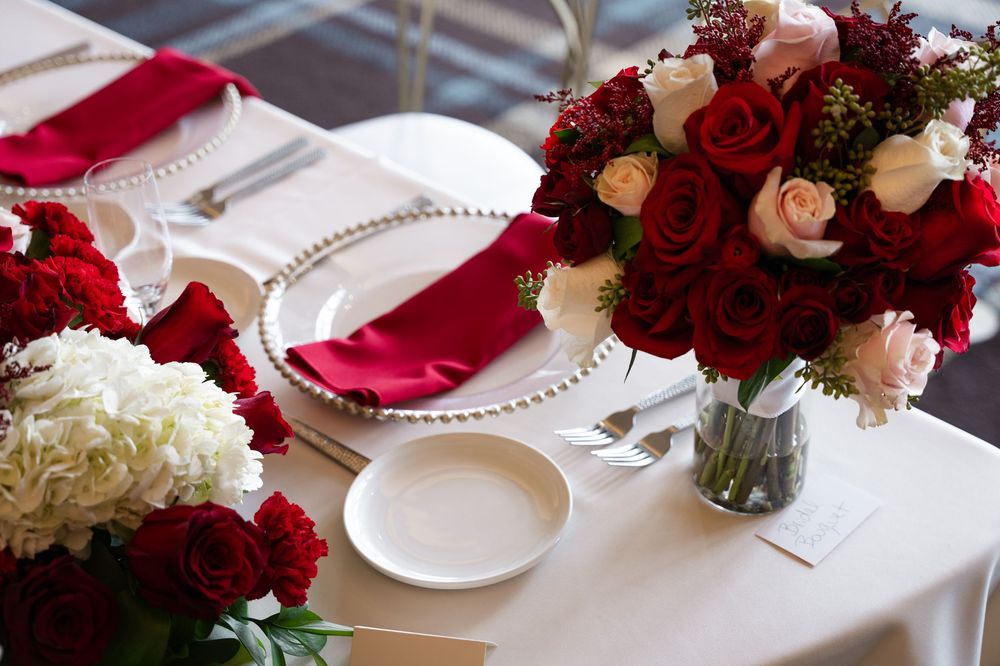 Elegant table settings with red and white roses in vases alongside fine china and crystal glassware.