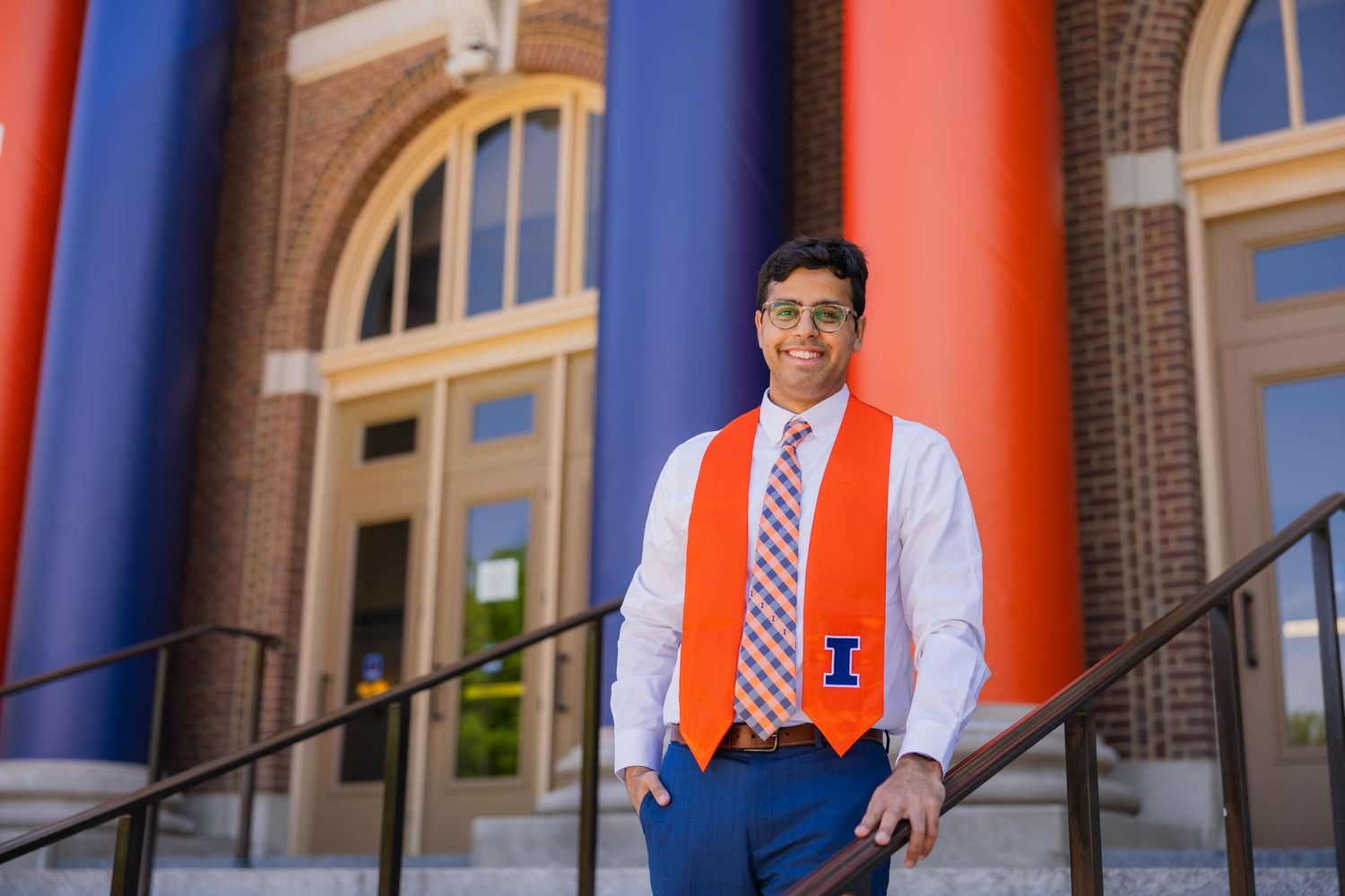 Male UIUC graduate leaning at Foellinger with orange and blue pillars in the back