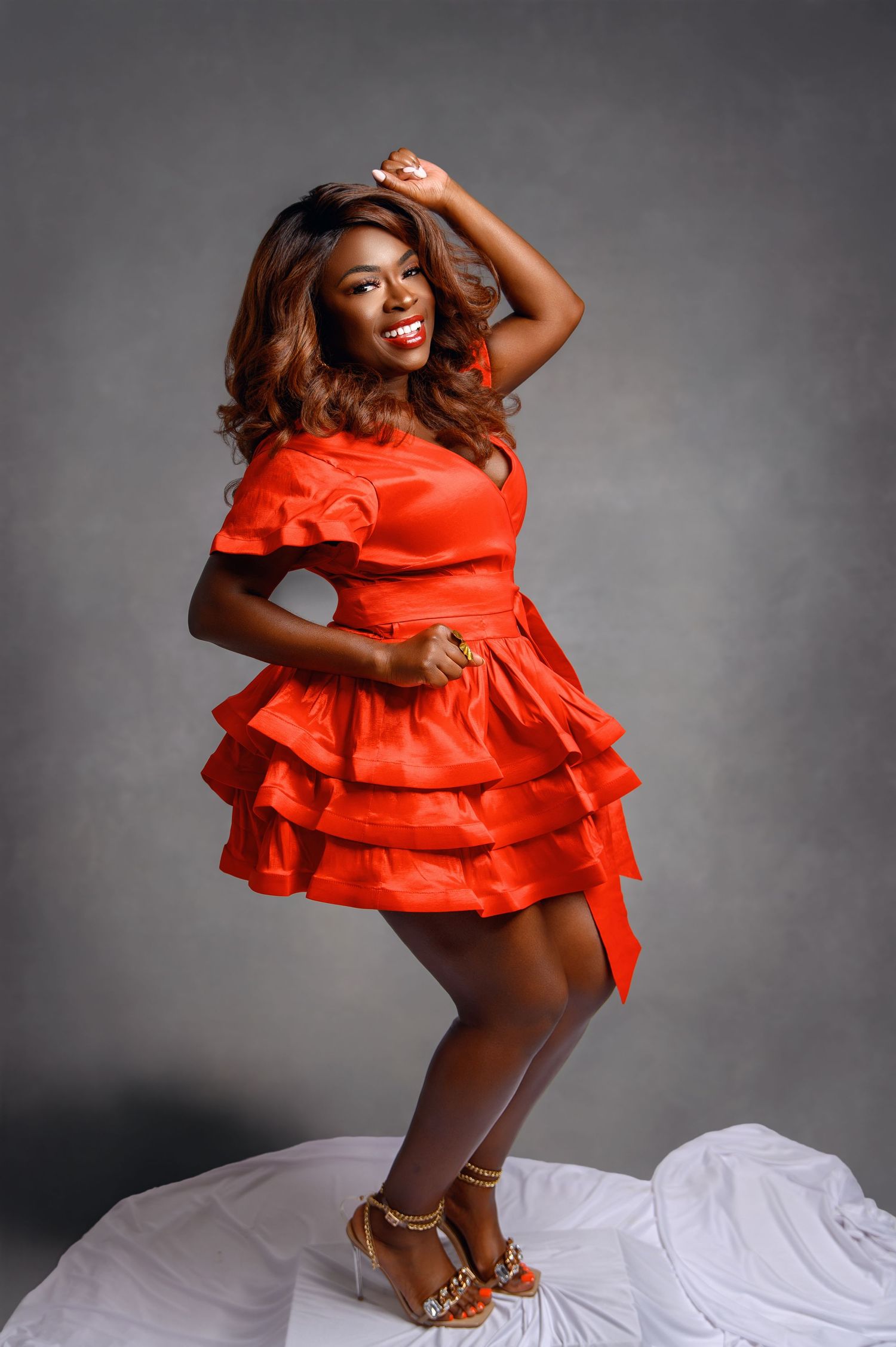 A fashion model poses in a vibrant red ruffled dress against a grey background in a dynamic photo series.