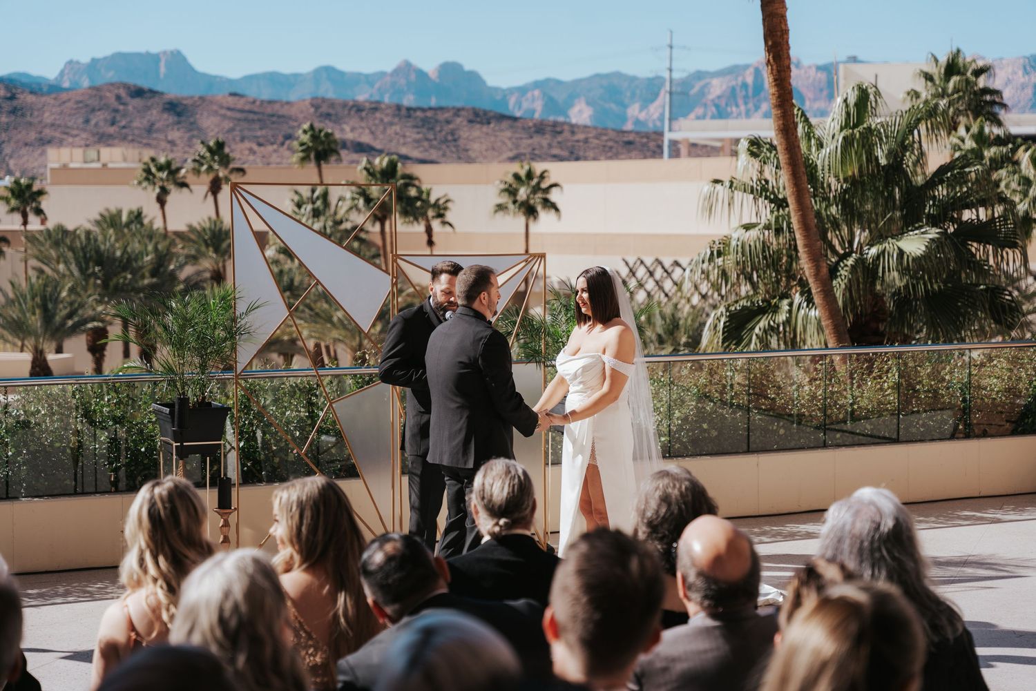 Wedding ceremony taking place outdoors with desert mountains and palm trees in the background.