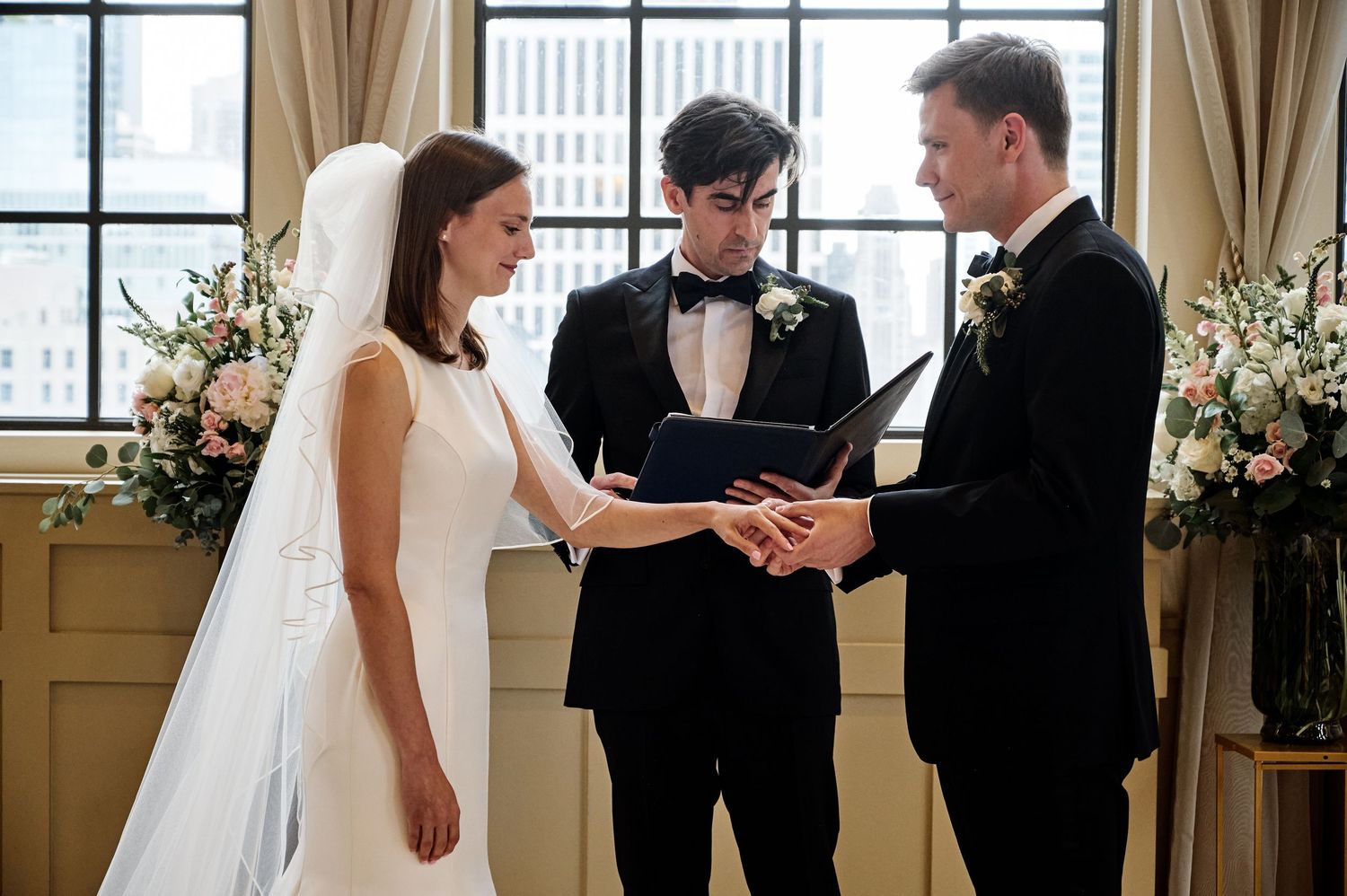 Elegant wedding ceremony moment with bride and groom exchanging rings in front of floral arrangements.