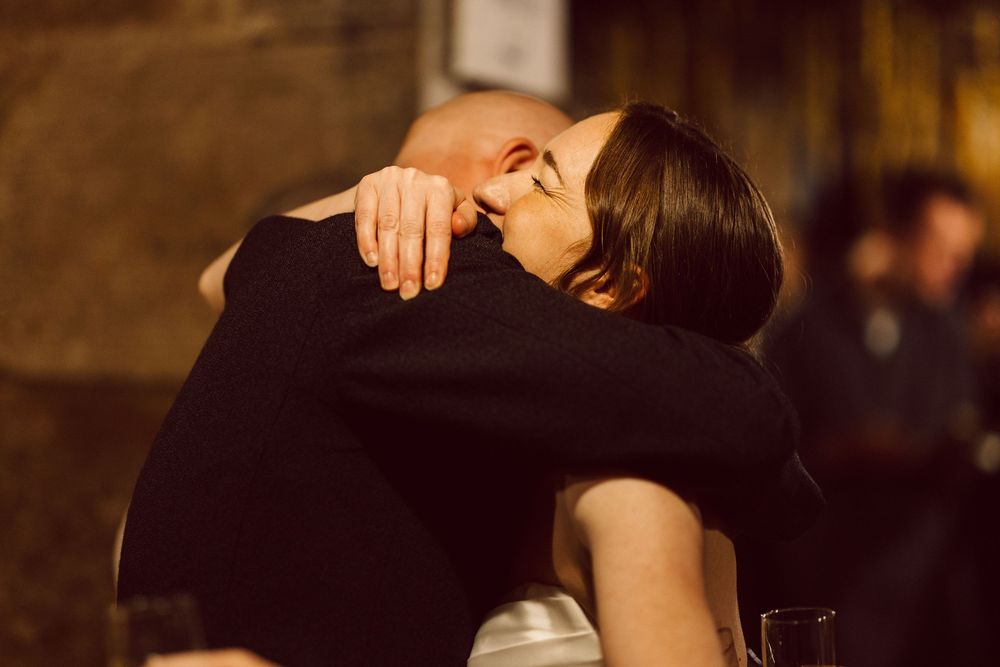 A couple in formal attire dance together in an intimate embrace on a dimly lit dance floor.