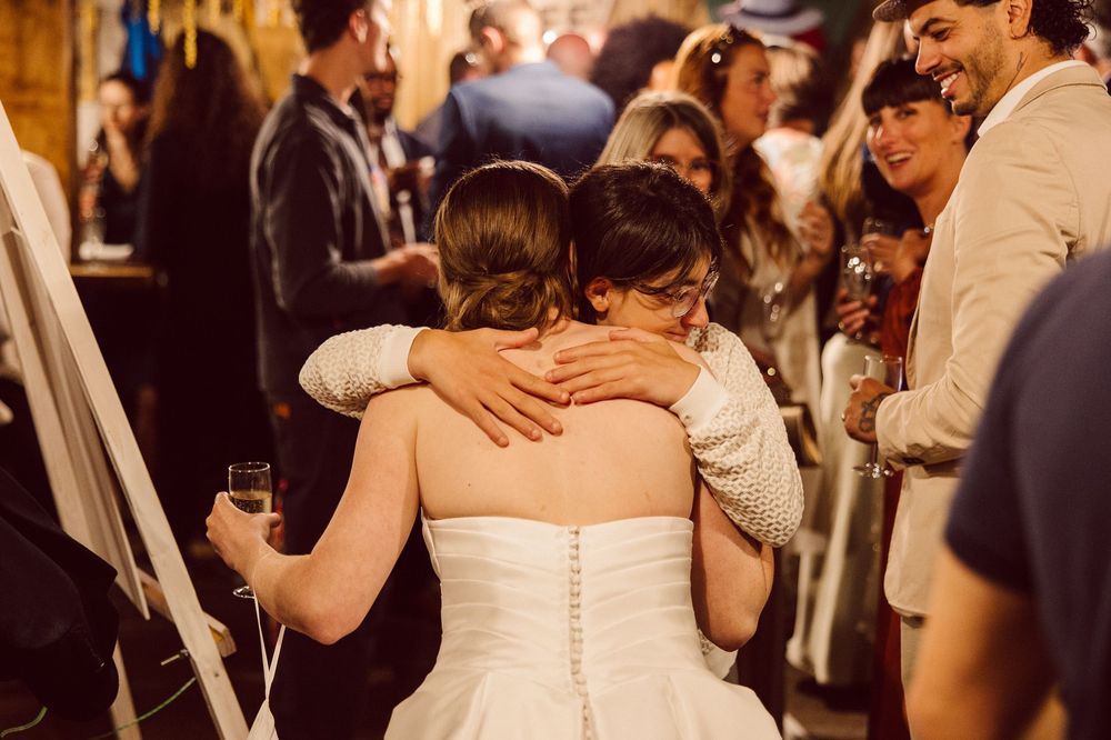 Joyful wedding celebration with people dancing and embracing on a crowded dance floor at a reception.