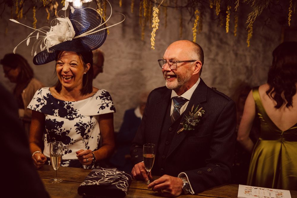 Wedding guests enjoy dancing and celebrating together at a dimly lit reception venue with decorative lighting.