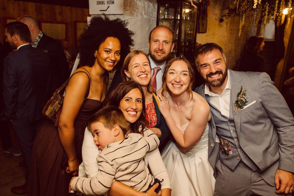 A group of friends laugh and embrace while socializing at a dimly lit bar or restaurant.