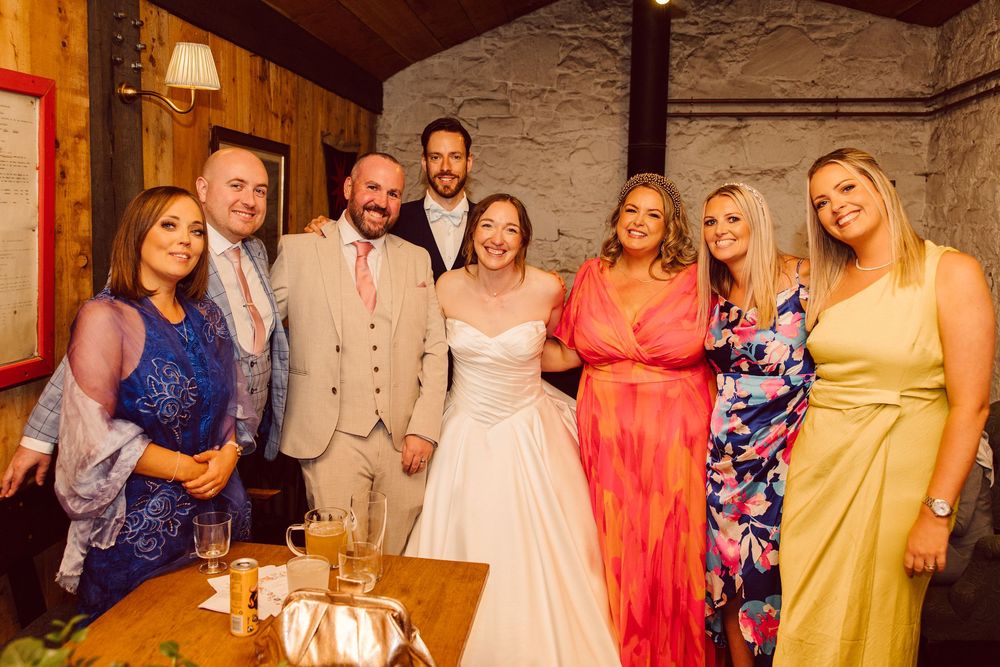 A group of people in colorful formal attire posing together at an indoor venue with stone walls and warm lighting.