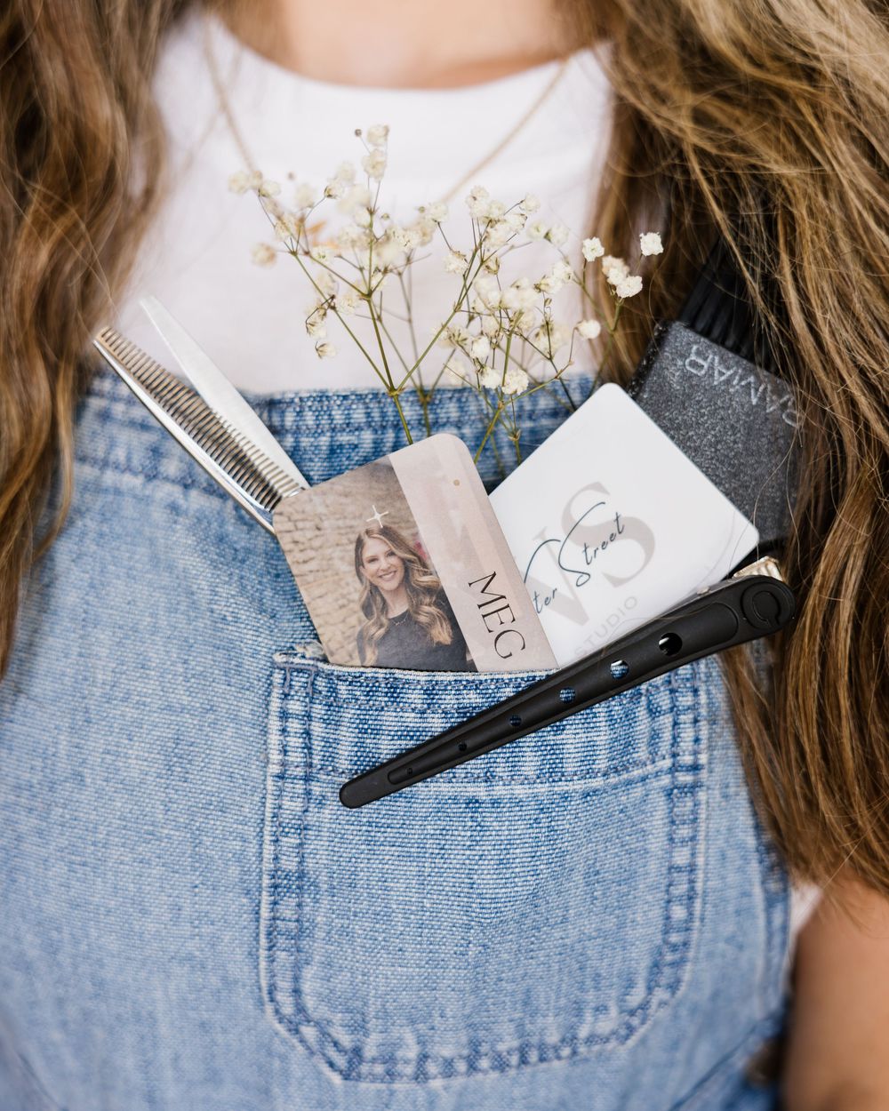 Close-up of denim overalls pocket with hair clips and dried baby's breath flowers as decorative accessories.